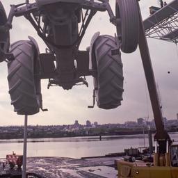 Crane lifting gray tractor.