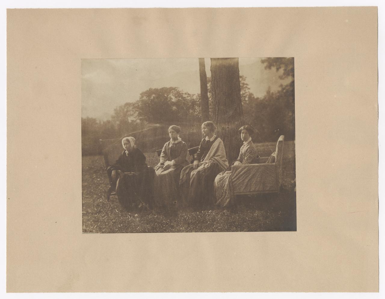 Four women seated by a tree.