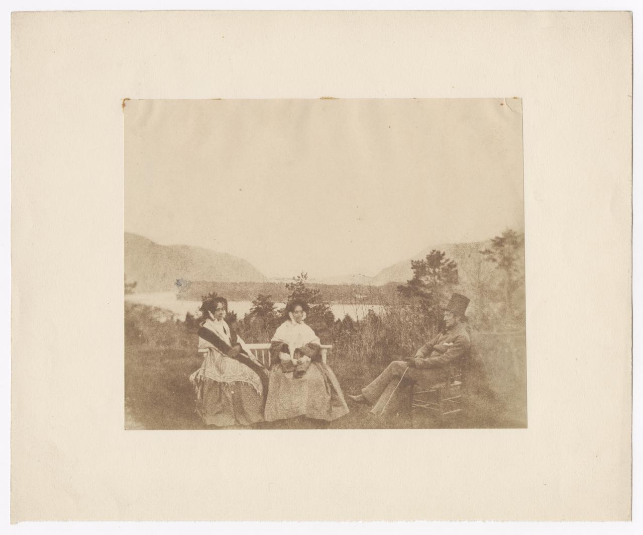 Two women and one man seated by the water.