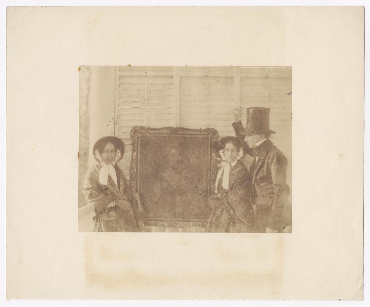 Two women and a man posing next to a painting.