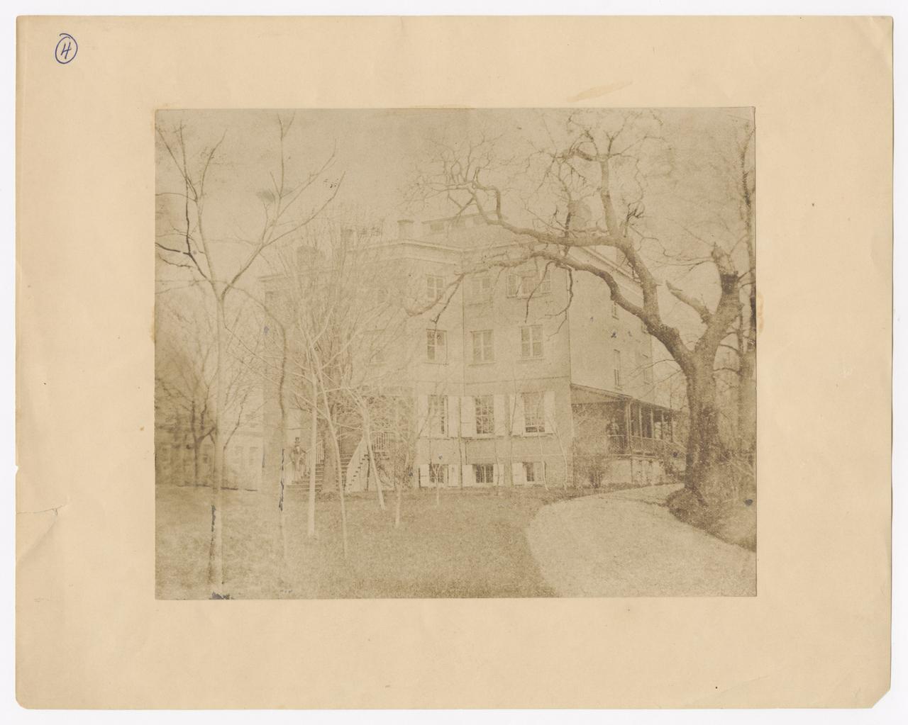 View of Chelsea house with a man standing on the steps and another man standing on the porch.