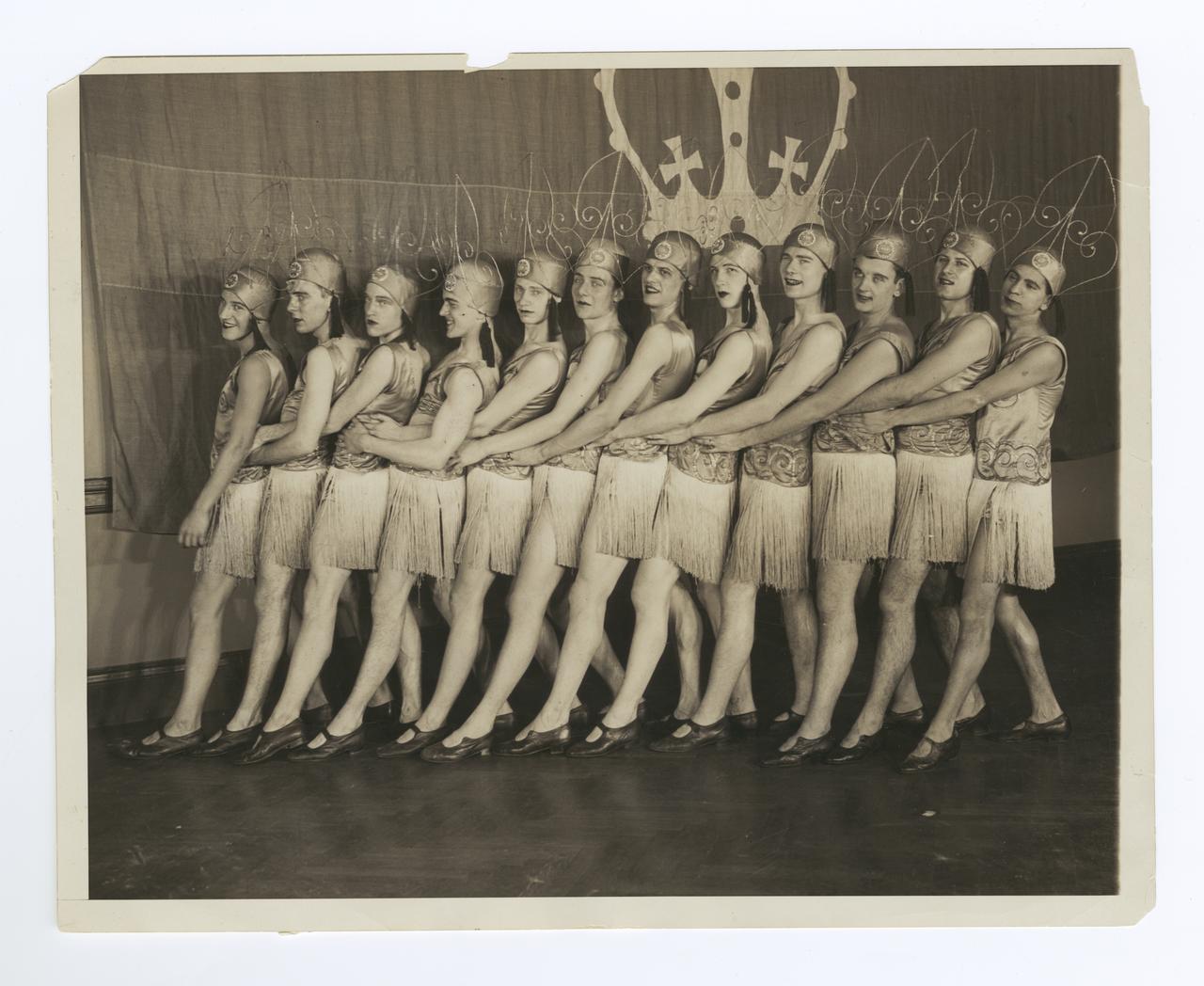 Image of the 1929 Varsity Show pony ballet. A group of men in a line made to look like women wearing fringed dresses and headdresses.