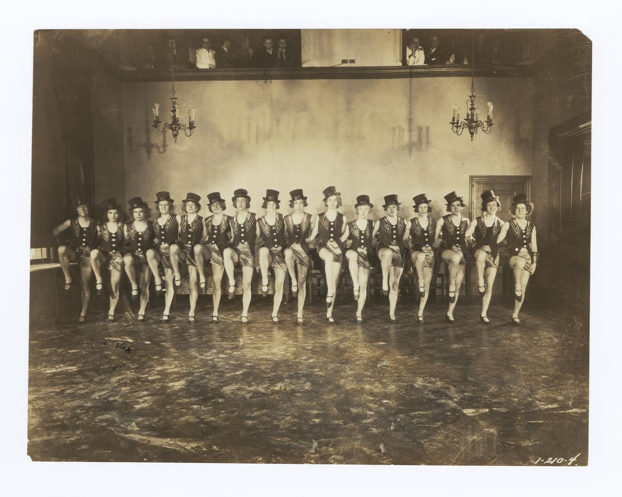 Image of 1931 Varsity Show pony ballet.  A group of men in a kick line made to look like women wearing top hats and short dresses.